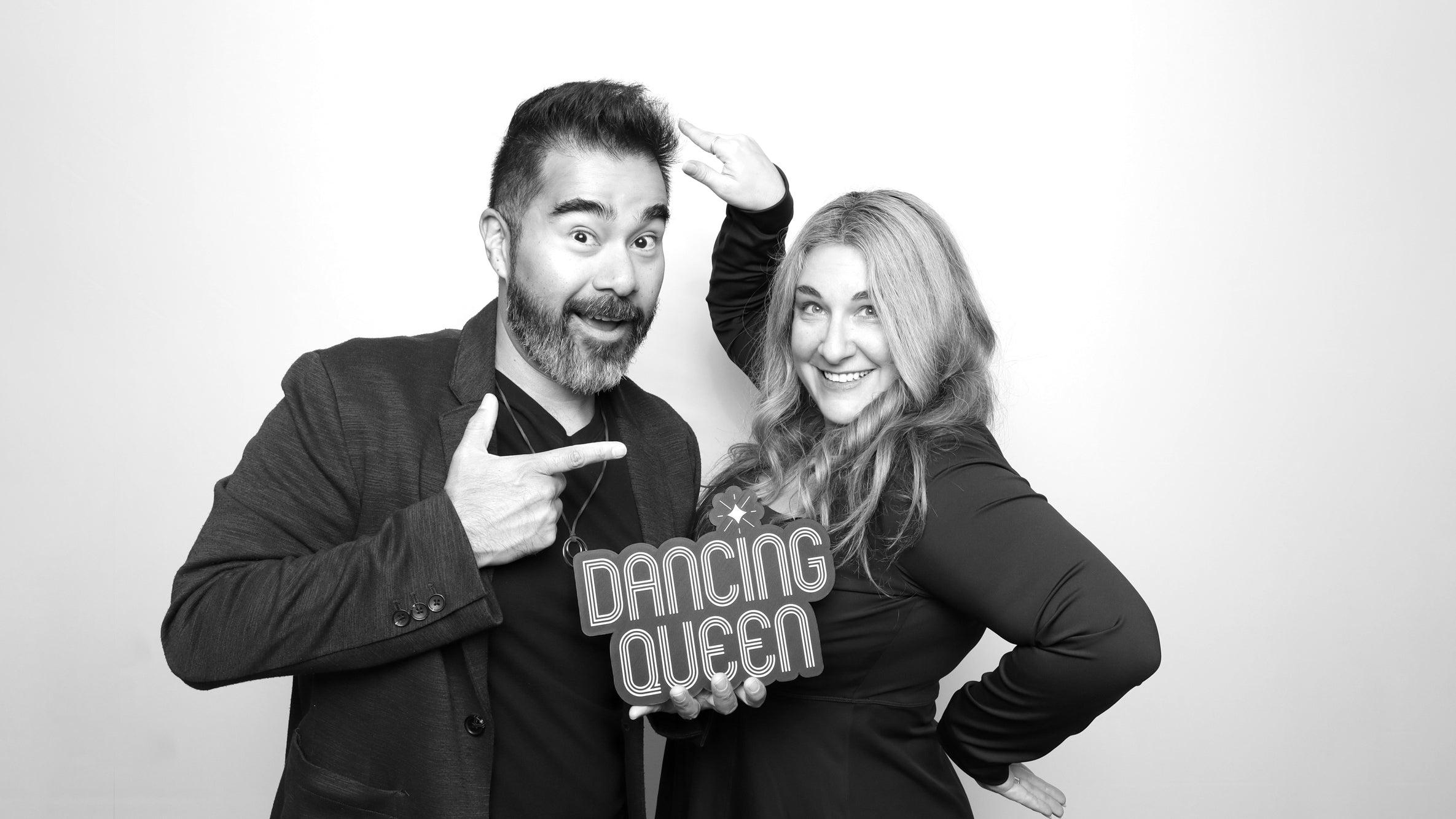 Two people posing with a 'Dancing Queen' sign in a black and white photo booth setting.
