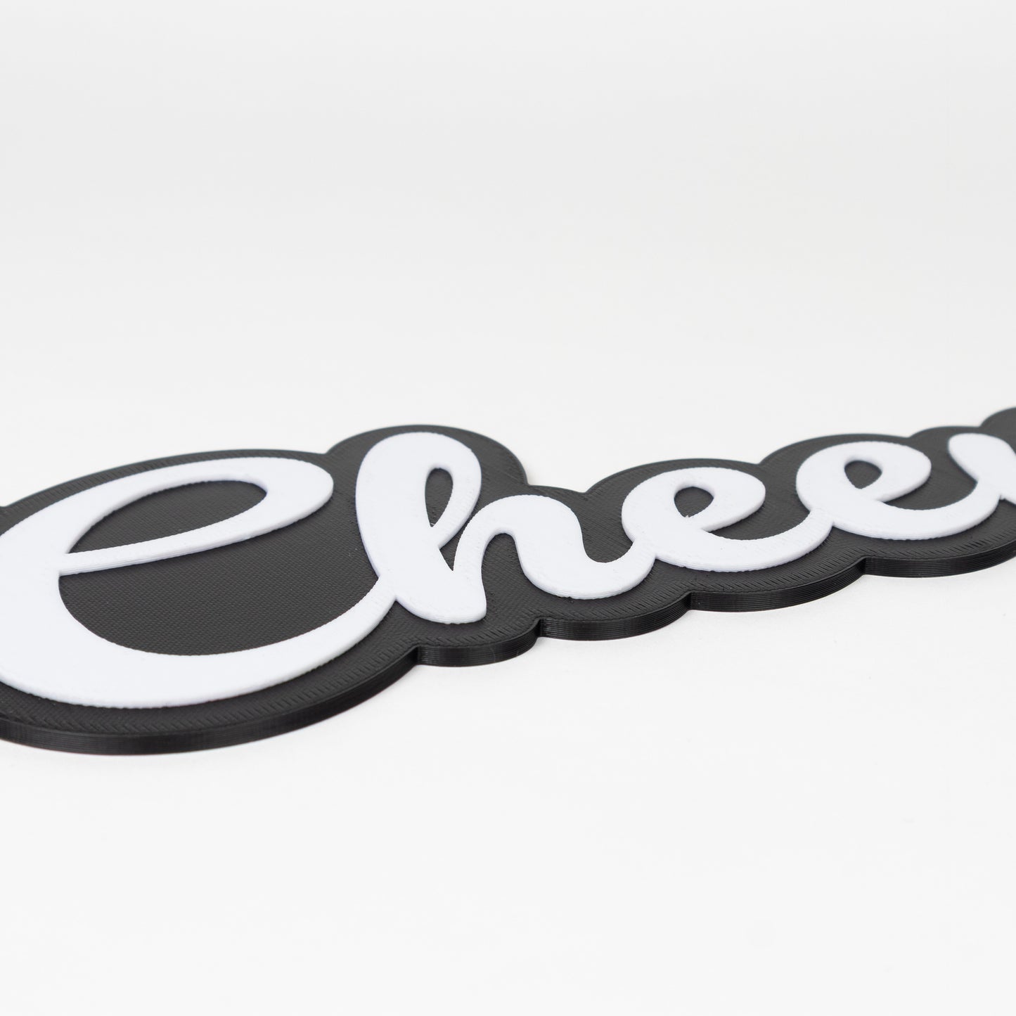 "Cheers!" photo booth prop sign with a matte black base and raised white lettering on a white background.