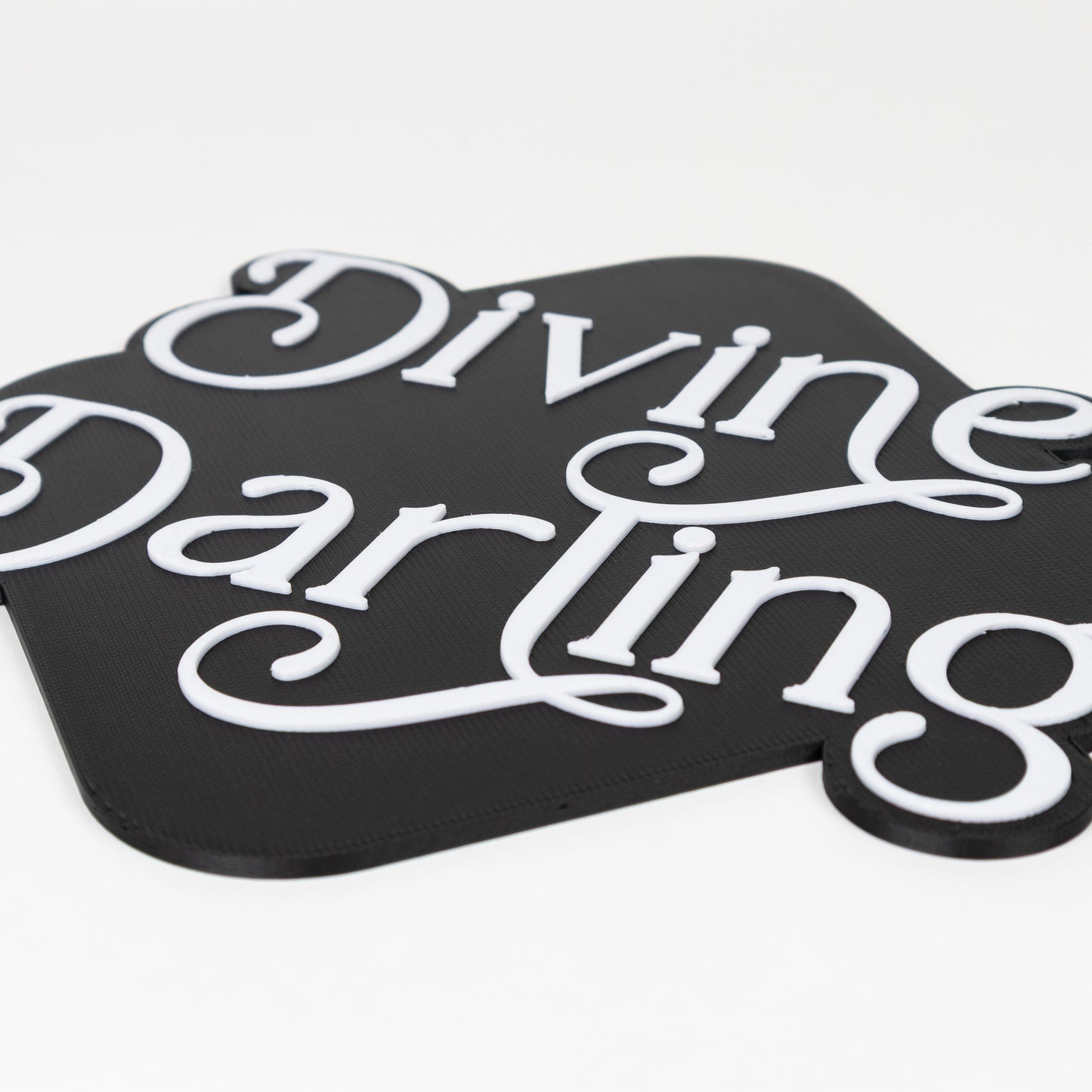 Black and white 'Divine Darling' photo booth prop sign on a white background. Close up shot of raised white lettering.