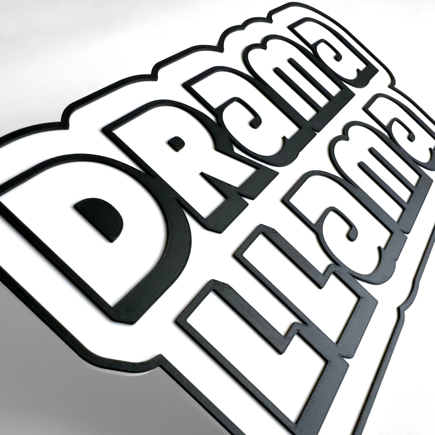 Close up of a black and white sign photo booth prop that says, "Drama Llama". Shows raised black lettering on a white base.