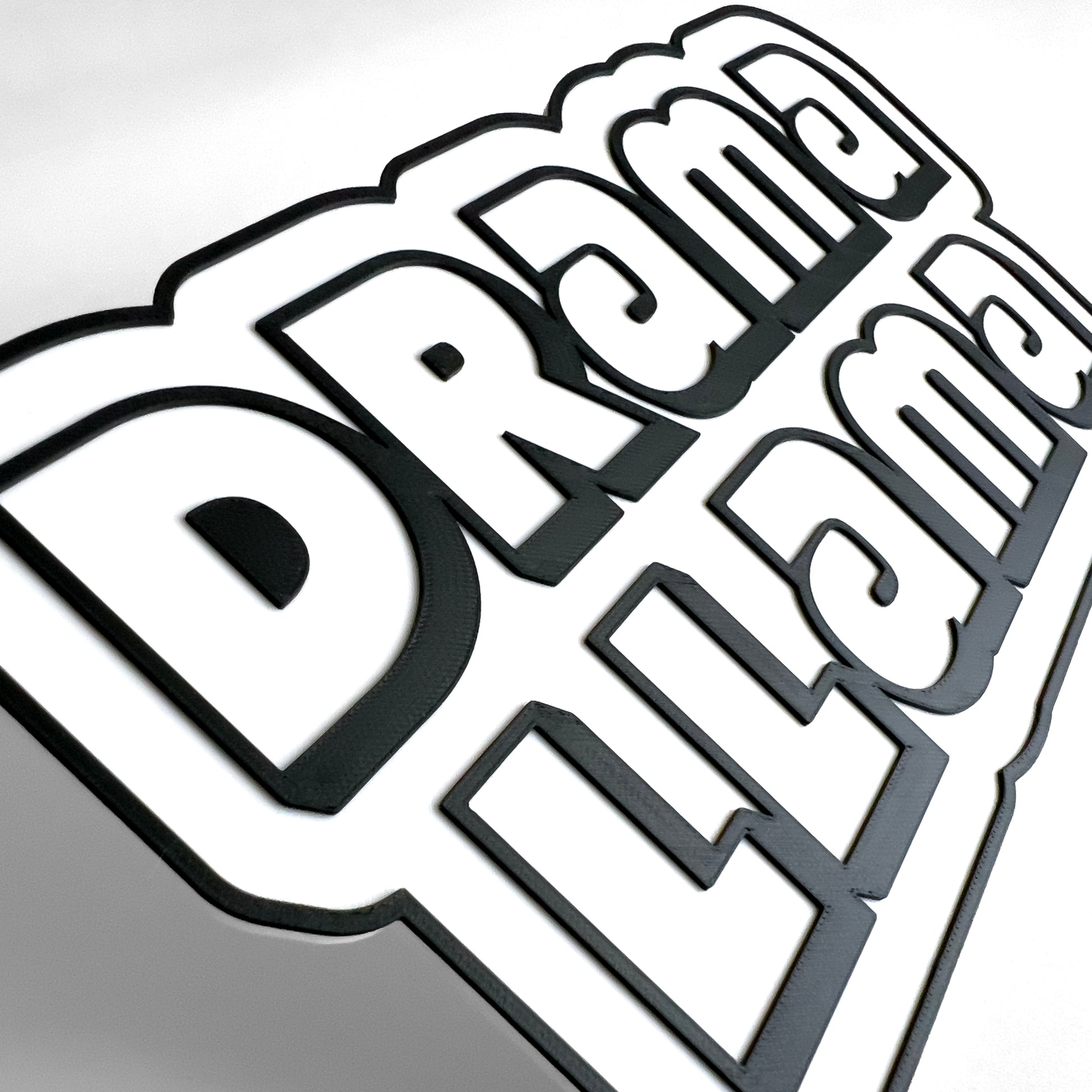Close up of a black and white sign photo booth prop that says, "Drama Llama". Shows raised black lettering on a white base.