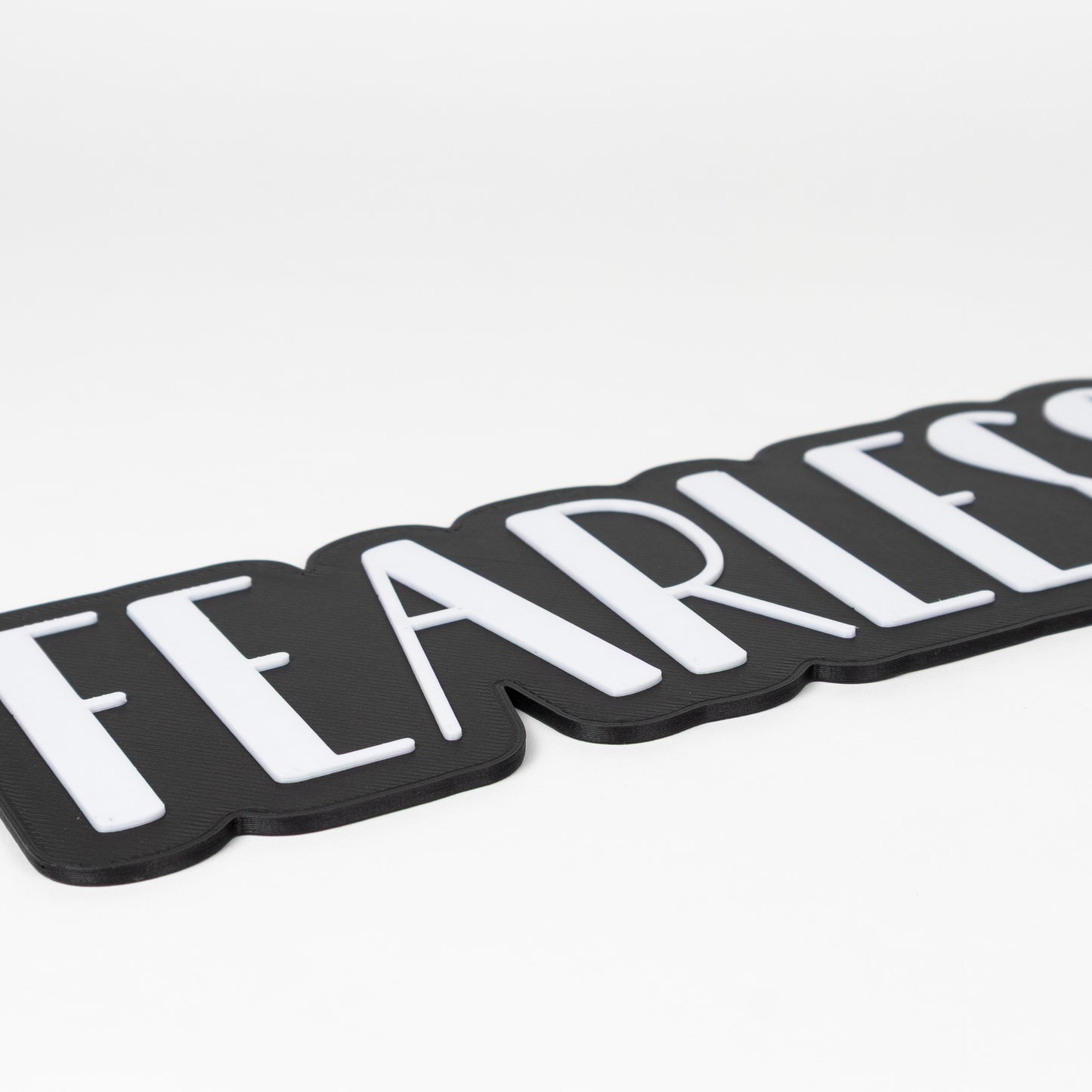 Close up shot of a black and white 'FEARLESS' photo booth prop sign on a white background. Features raised white lettering on a black base.
