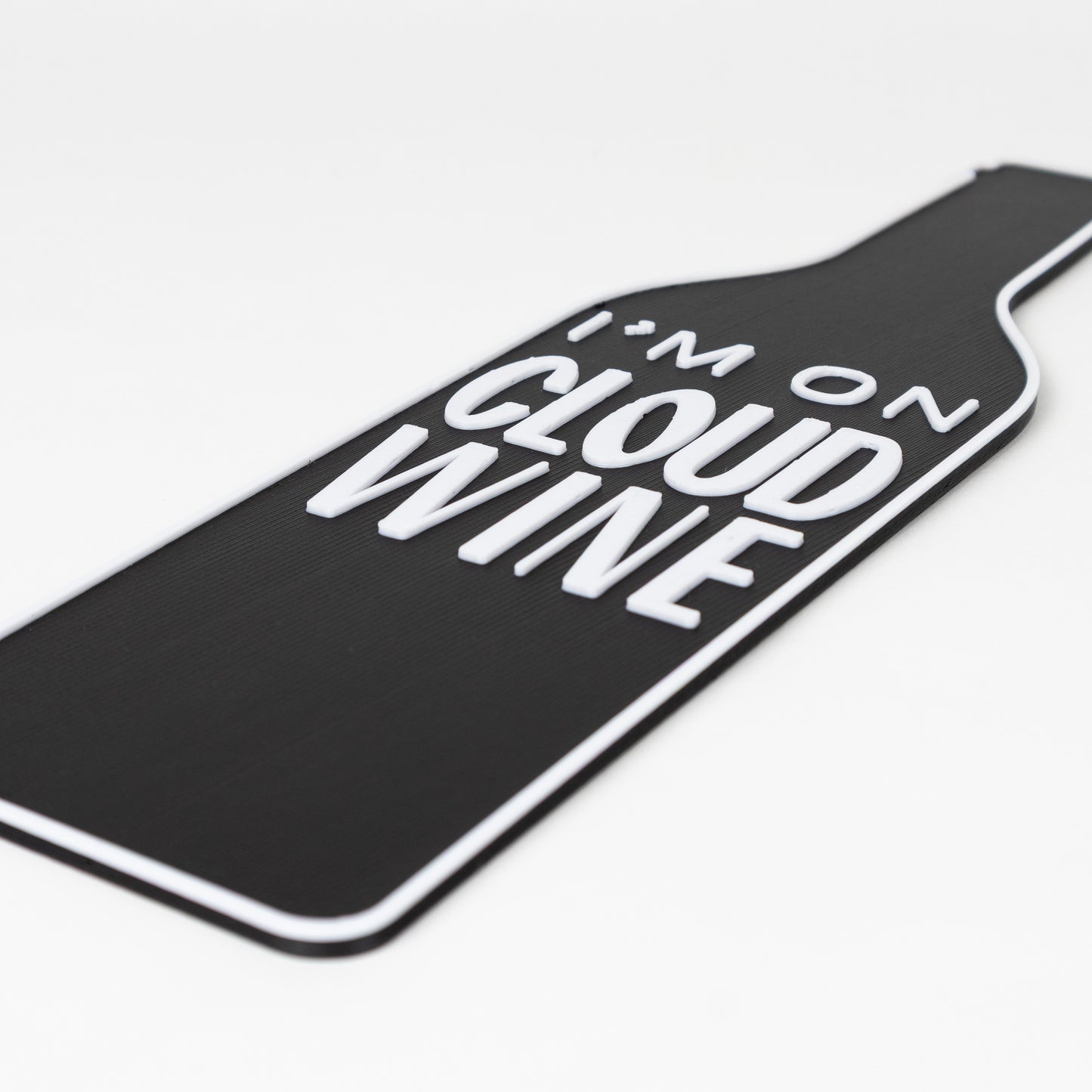 Close up shot of black wine bottle-shaped sign with raised text 'I'm on Cloud Wine'. Shot on a white background