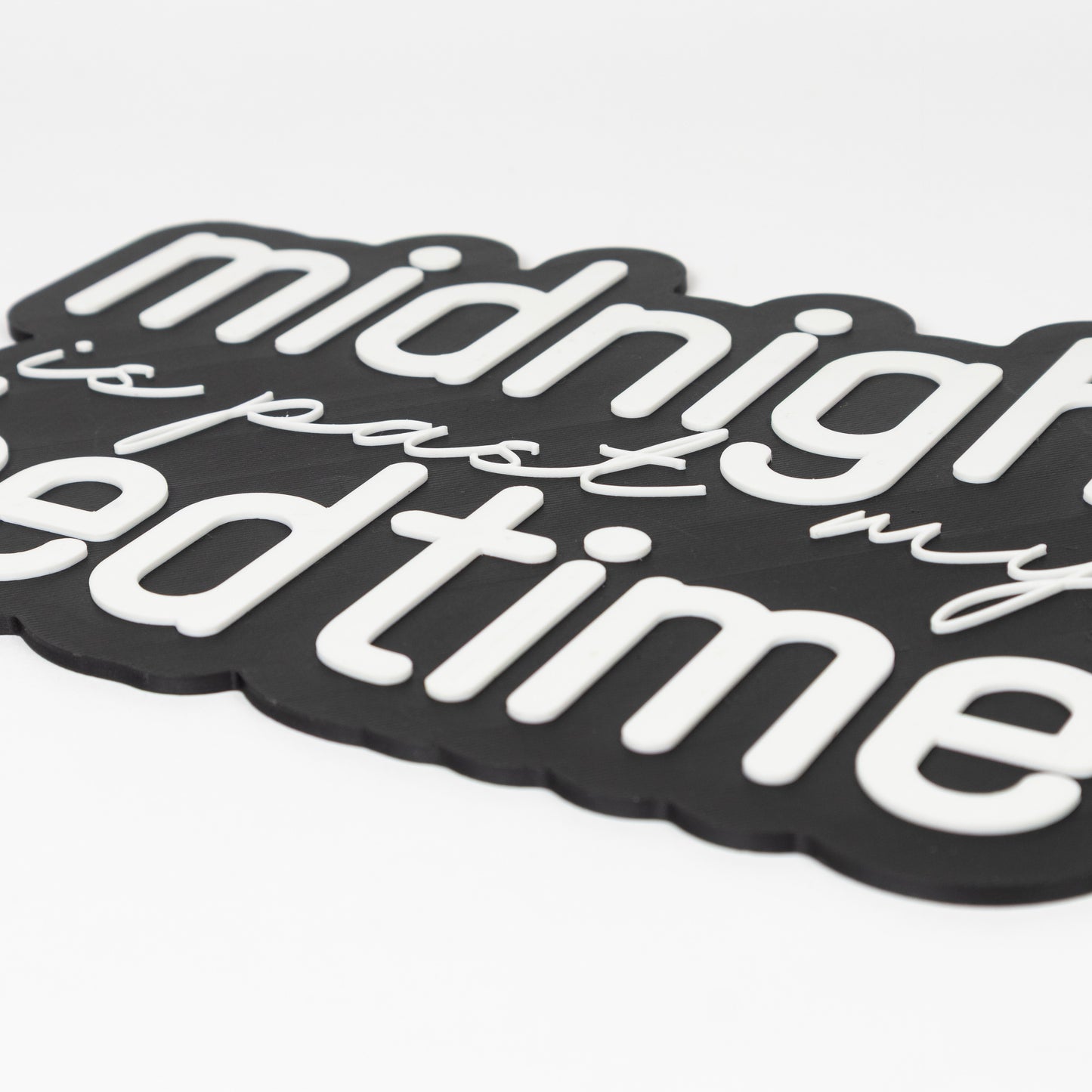 Close up photo of a photo booth prop sign that show raised white text. Black base with 'midnight is past my bedtime' text on a white background