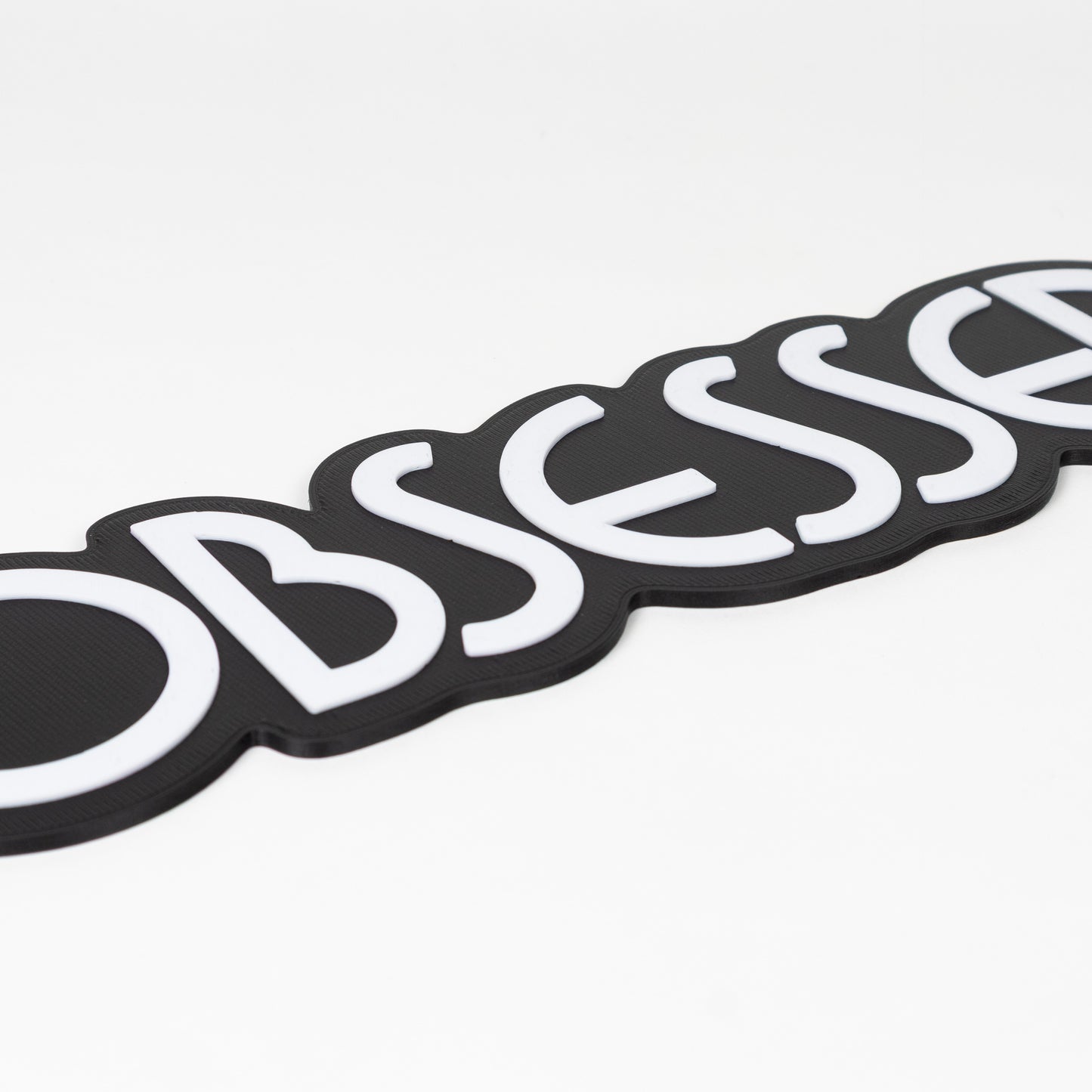 Close up of black and white "Obsessed" sign. Shows raised white text on a black base. Photo booth prop.