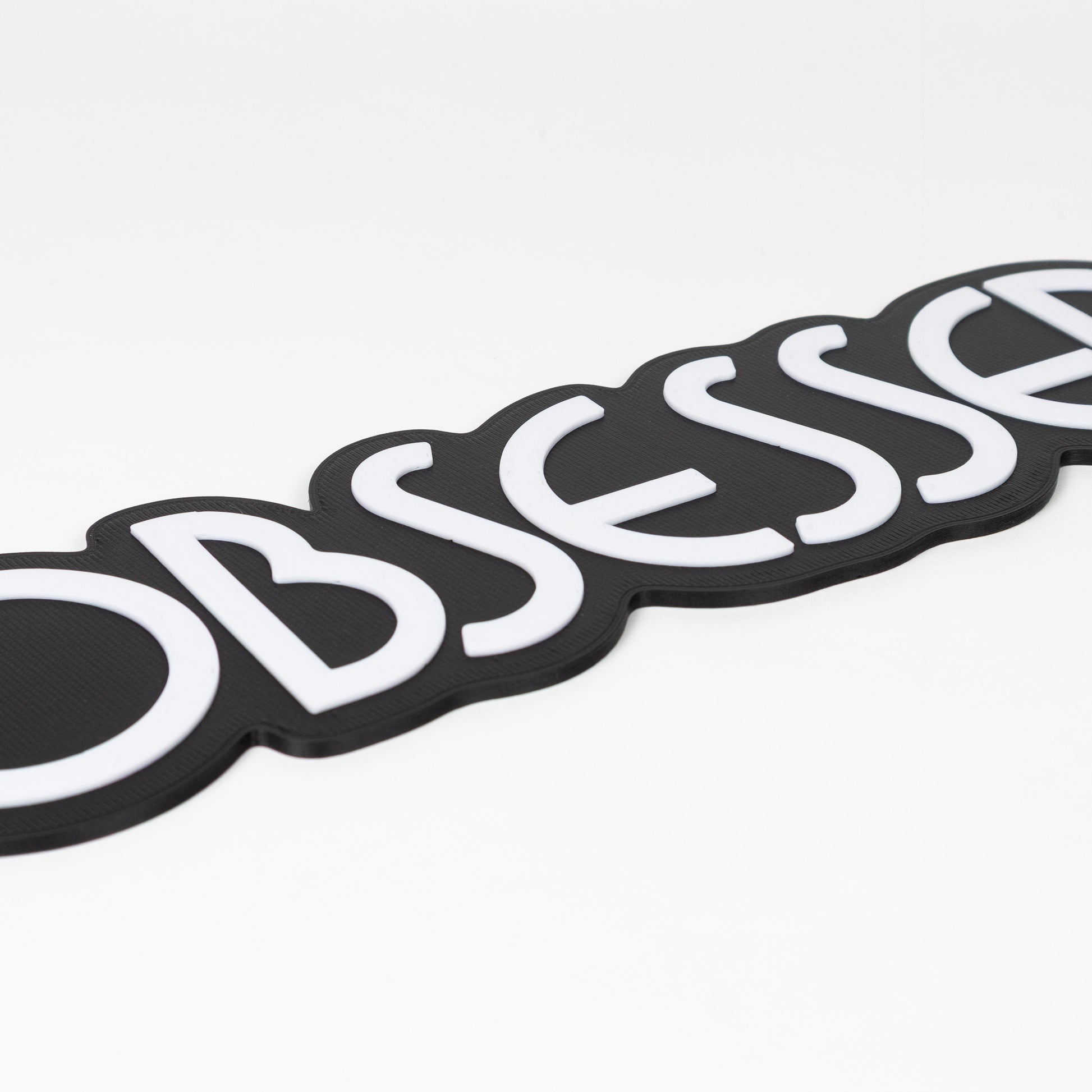 Close up of black and white "Obsessed" sign. Shows raised white text on a black base. Photo booth prop.