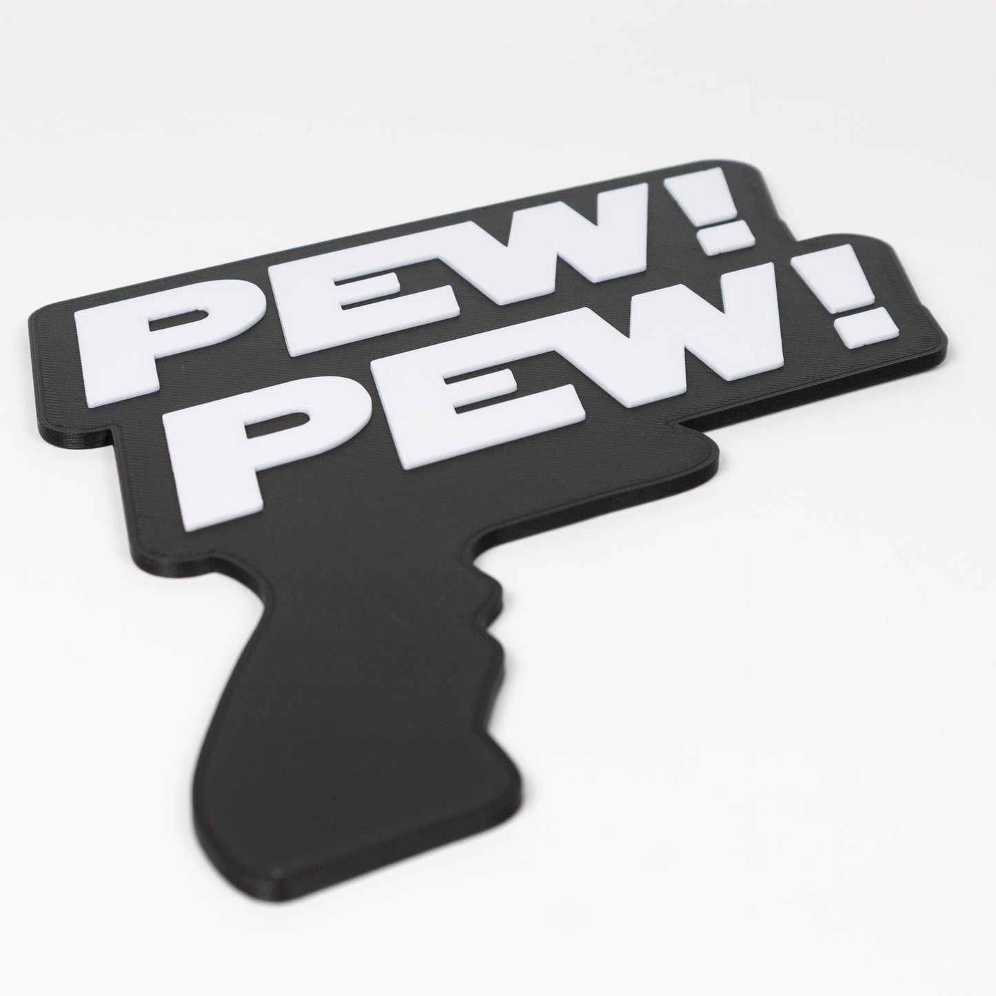 Close up of a black and white sign that says "Pew Pew!". Shows raised white text on a black base. Sign is in the shape of a Star Wars blaster. Photo booth prop.