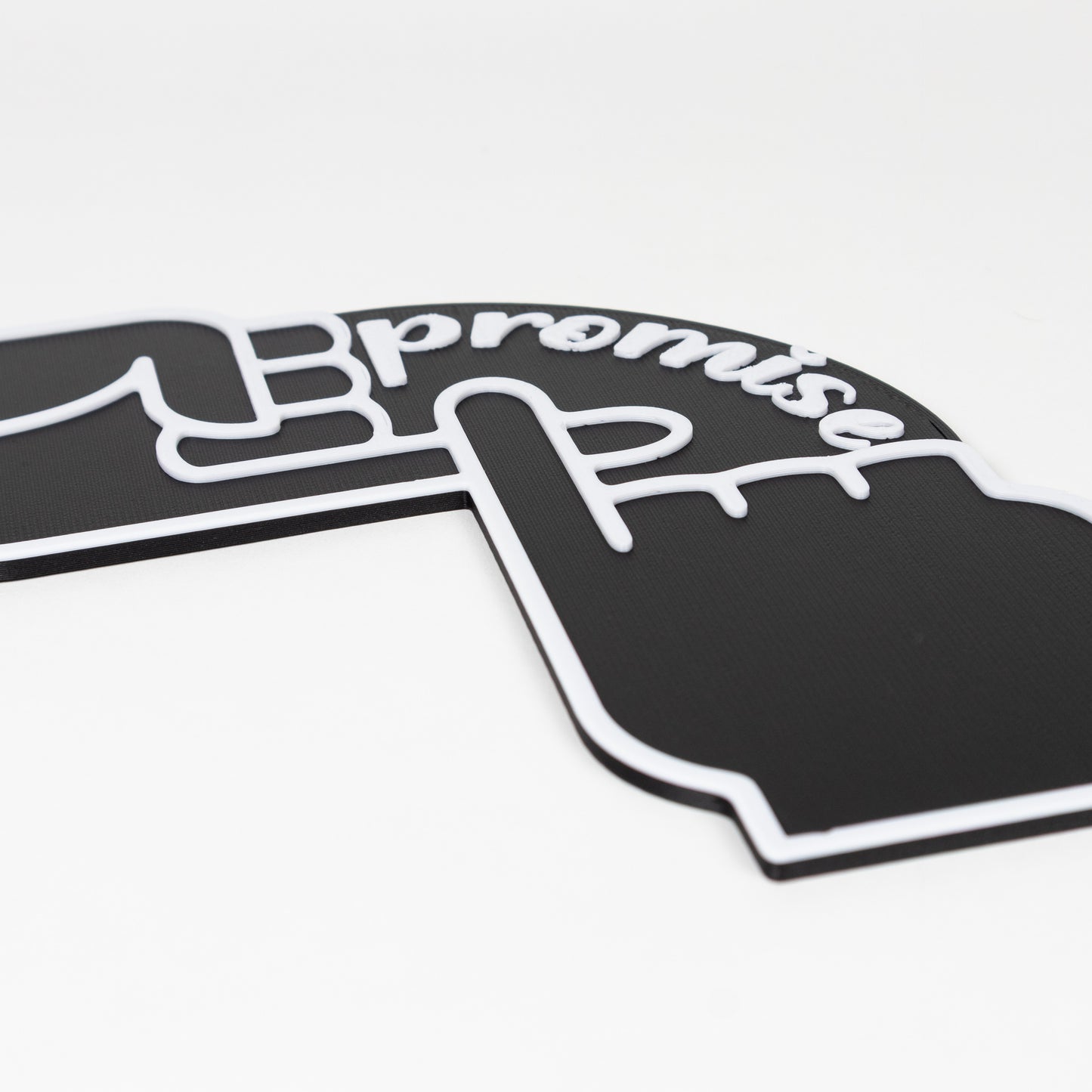 Close up of a black and white "Pinky Promise" sign. Shows raised white text and hand outlines on a black silouette. Photo booth prop.