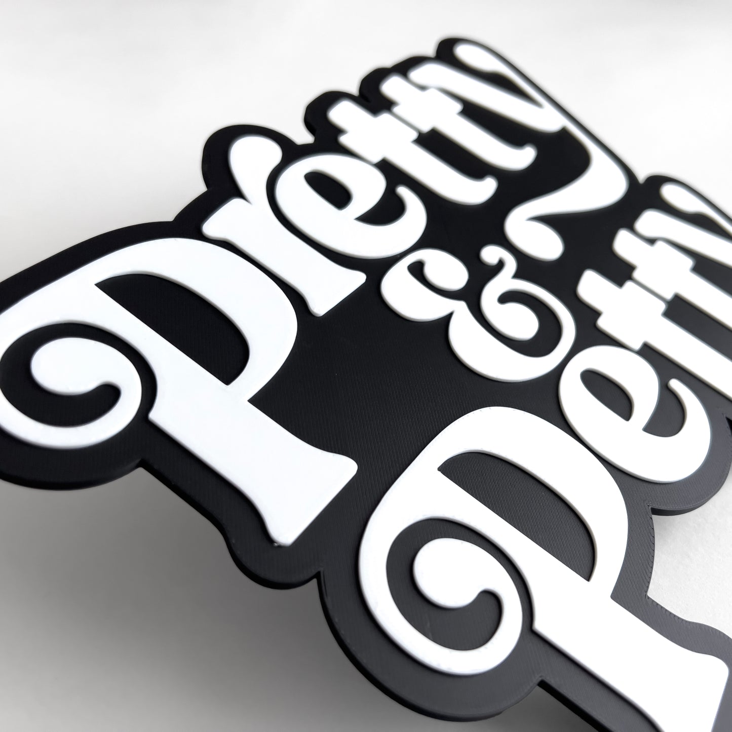 Close up of a black and white sign that says "Pretty and Petty". Shows raised white lettering.