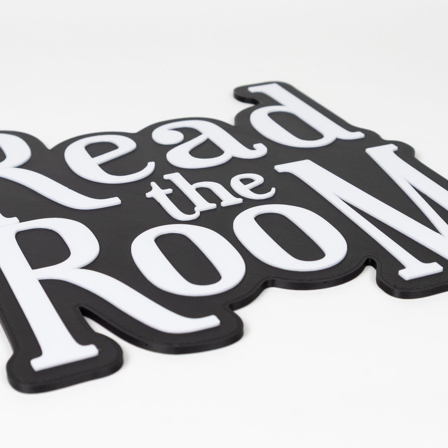 Close up of raised white text on a black base. Black and white "Read the Room" sign. Photo booth prop.