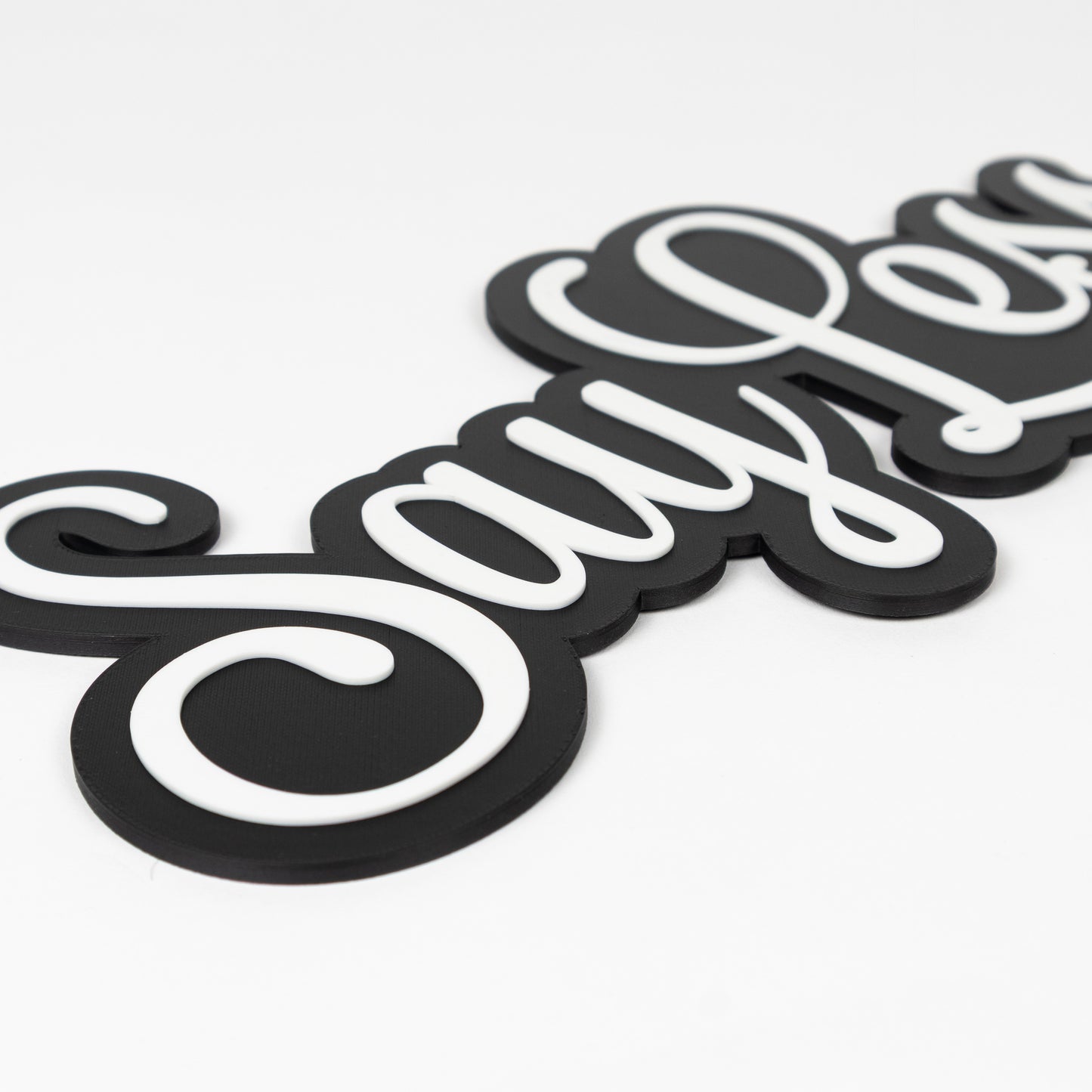 Close up of black and white "Say Less" sign. Shows raised white text on a black base. Photo booth party prop.
