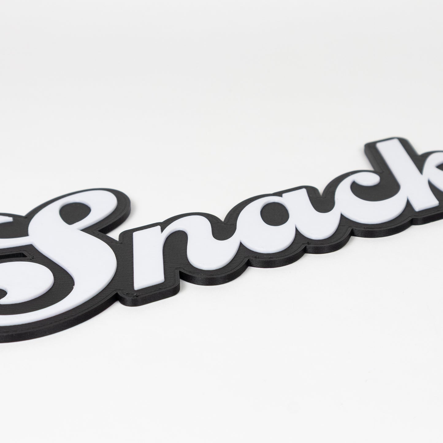 Close up of black and white flirty "Snack" sign. Shows raised white text on a black silhouette base. Photo booth prop.