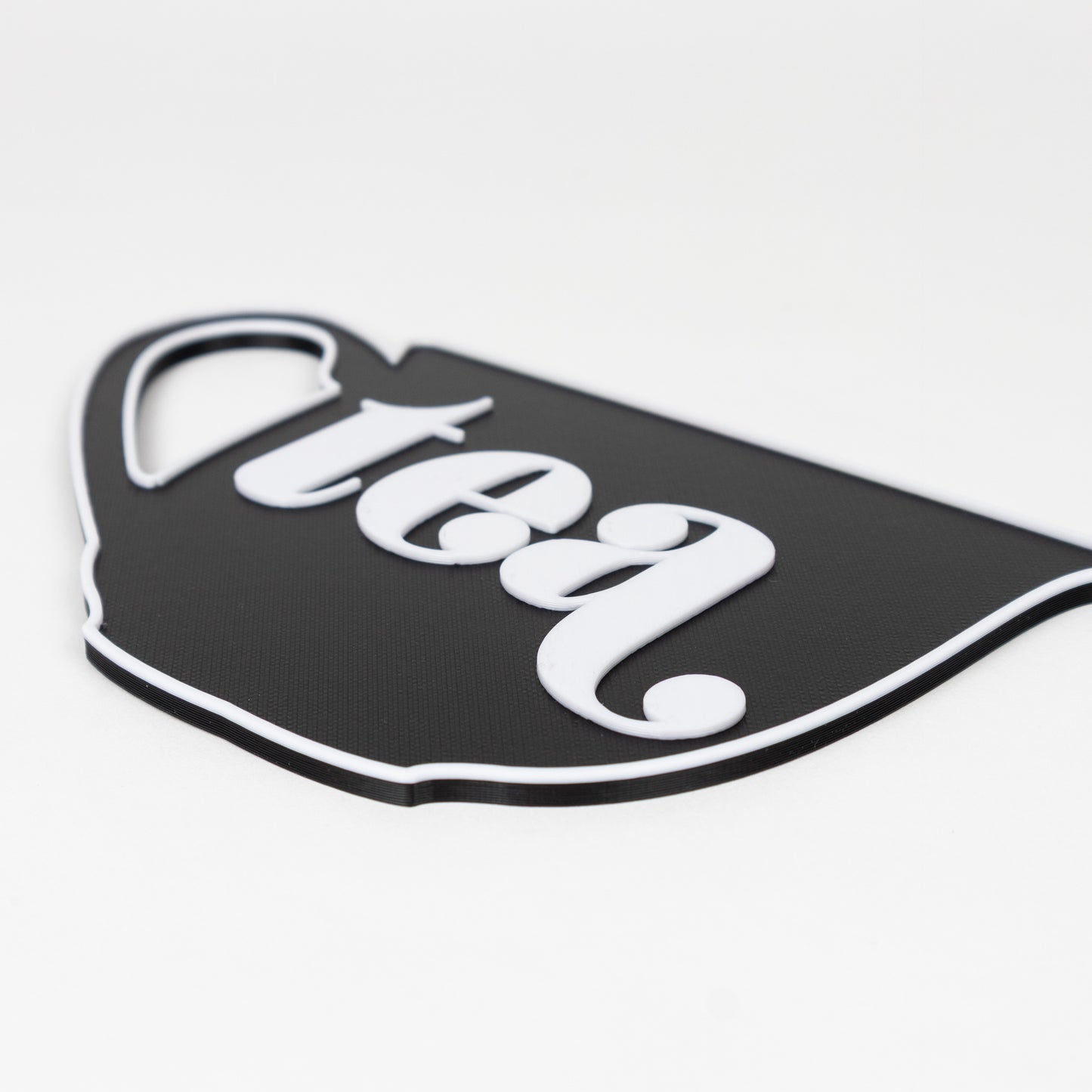 Close up photo of raised white text on a black base. Black and white sign in the shape of a tea cup that says, "tea". Photo booth prop.