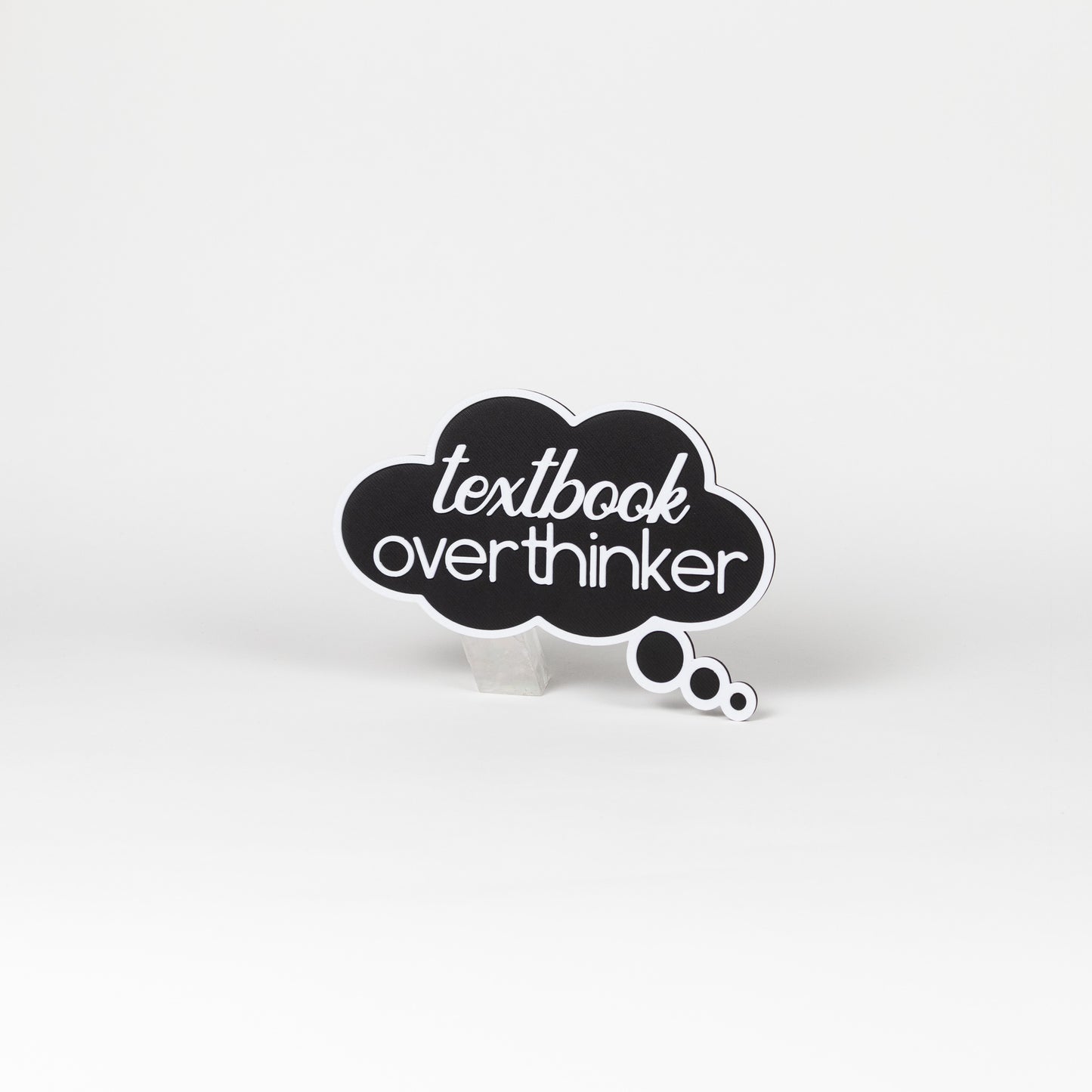Black thought bubble sign with 'textbook overthinker' text in white. Photo booth prop shot on a white background.