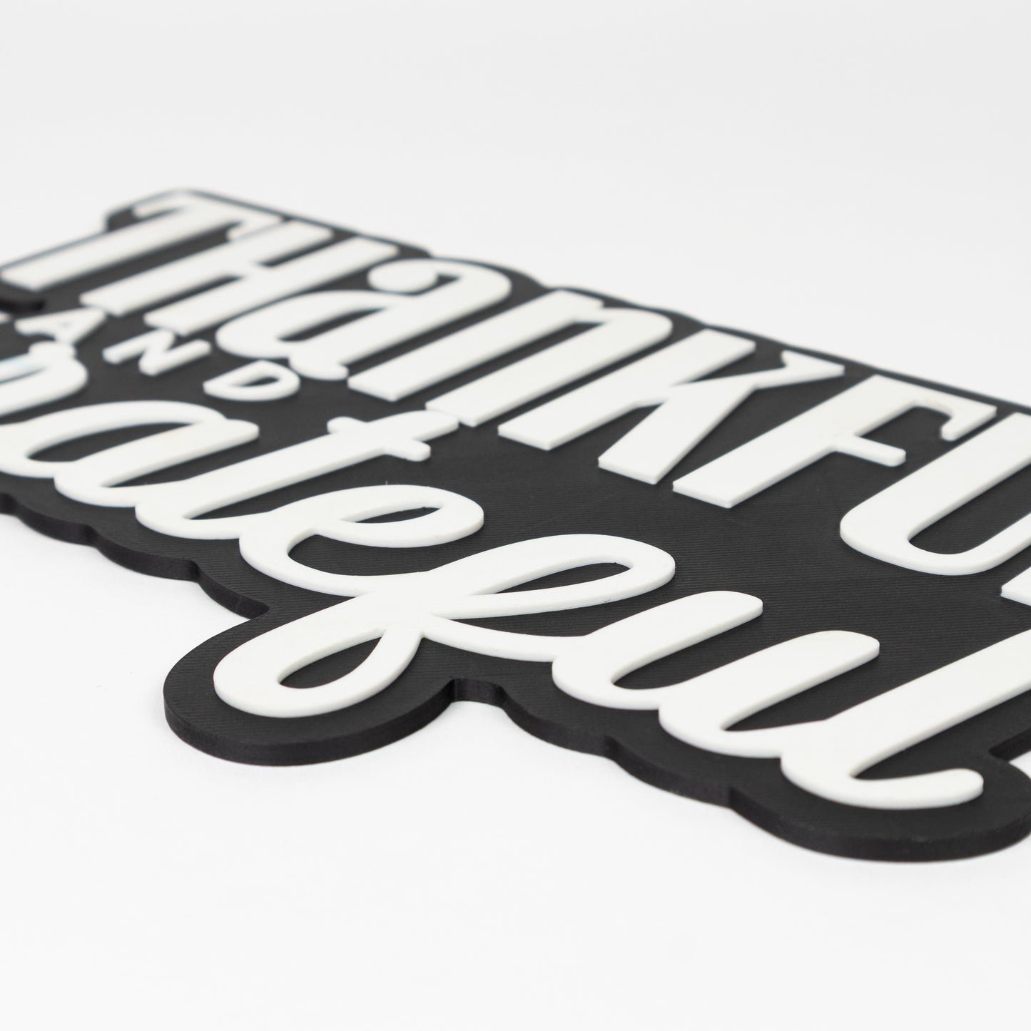 Close up of black and white "Thankful and Grateful" sign. Shows raised white text on a black base. Photo booth prop.