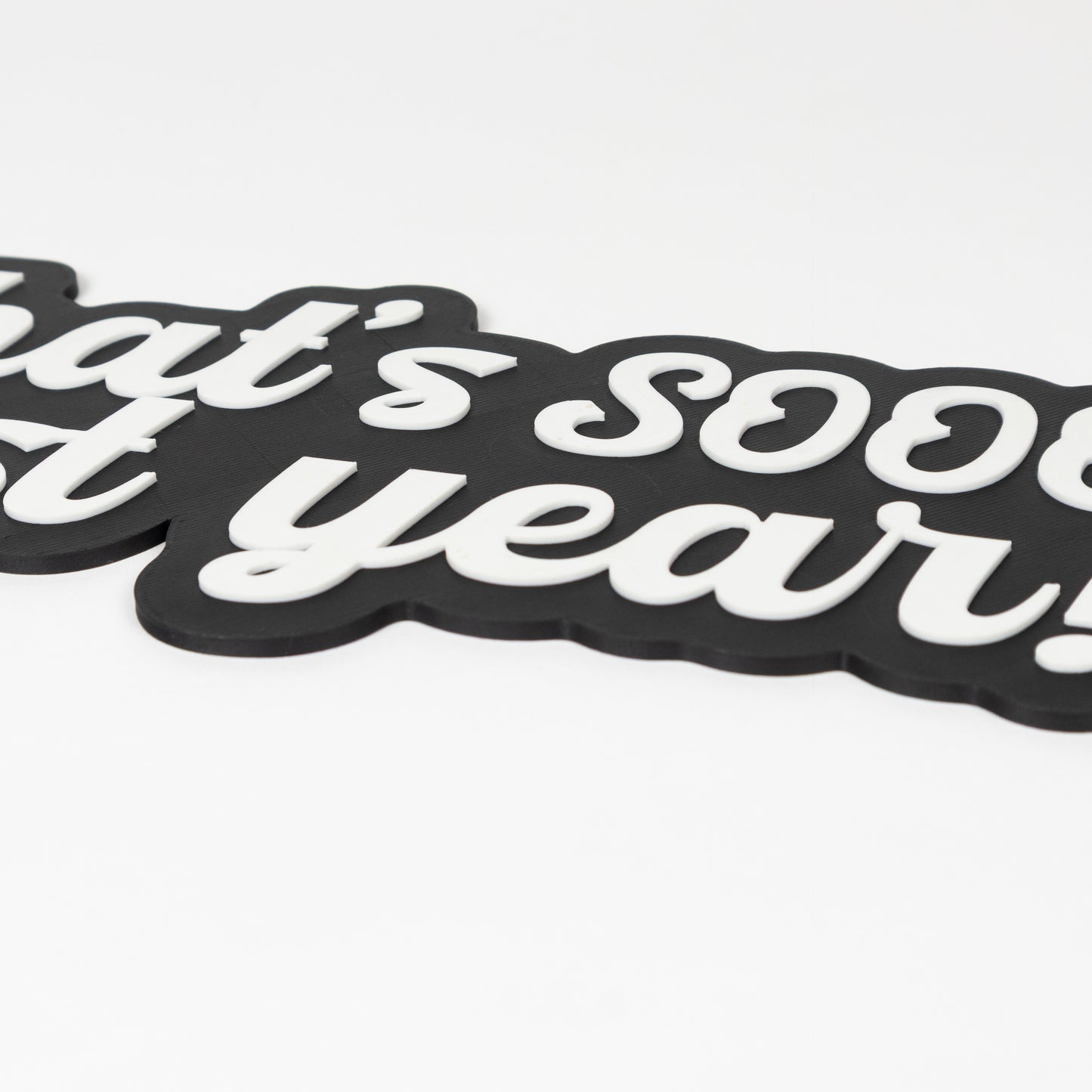 Close up of black and white sign that says, "That's Sooo Last Year!". Shows raised white text. NYE photo party prop.