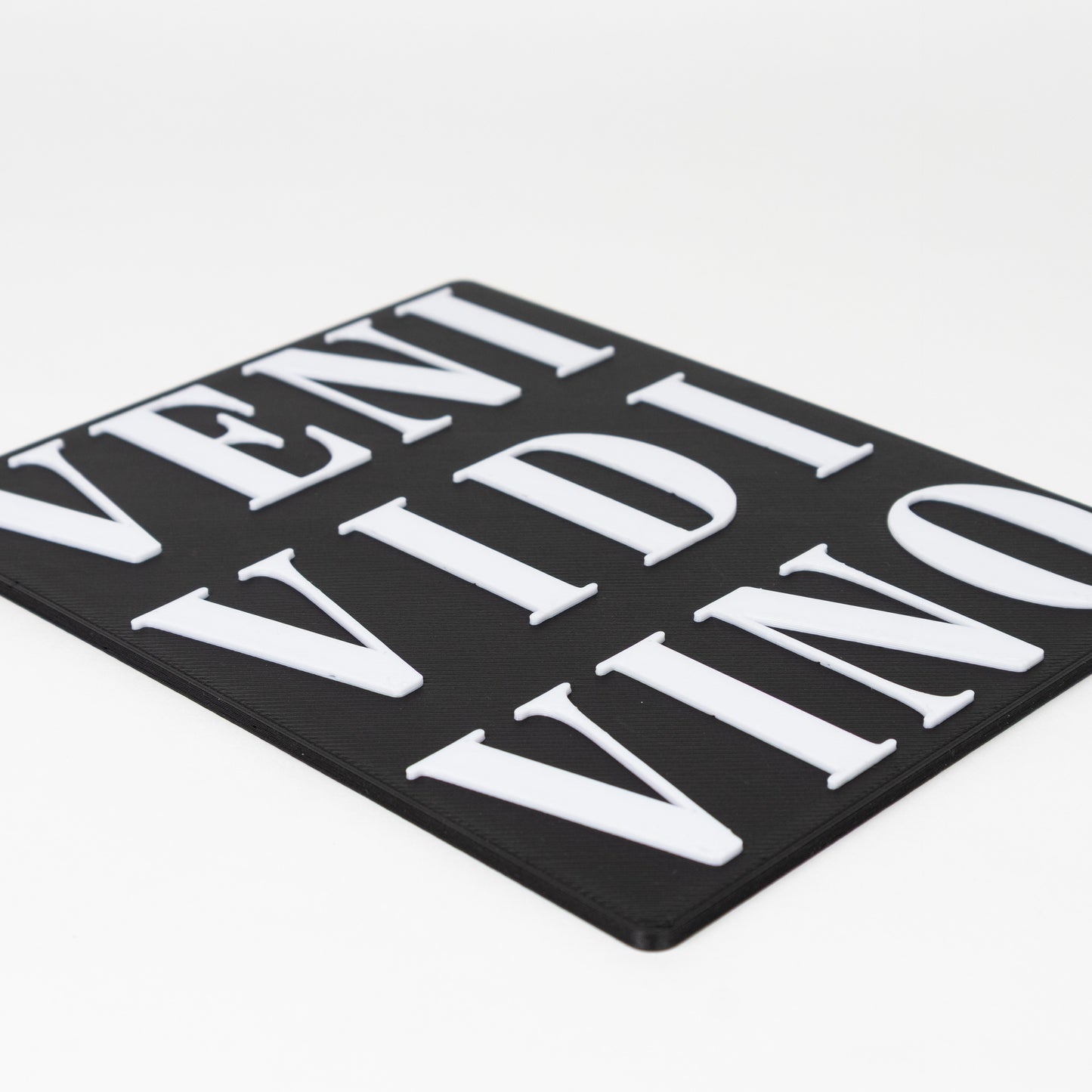 Close up of raised text of black sign with white text 'VENI VIDI VINO' shot on a white background