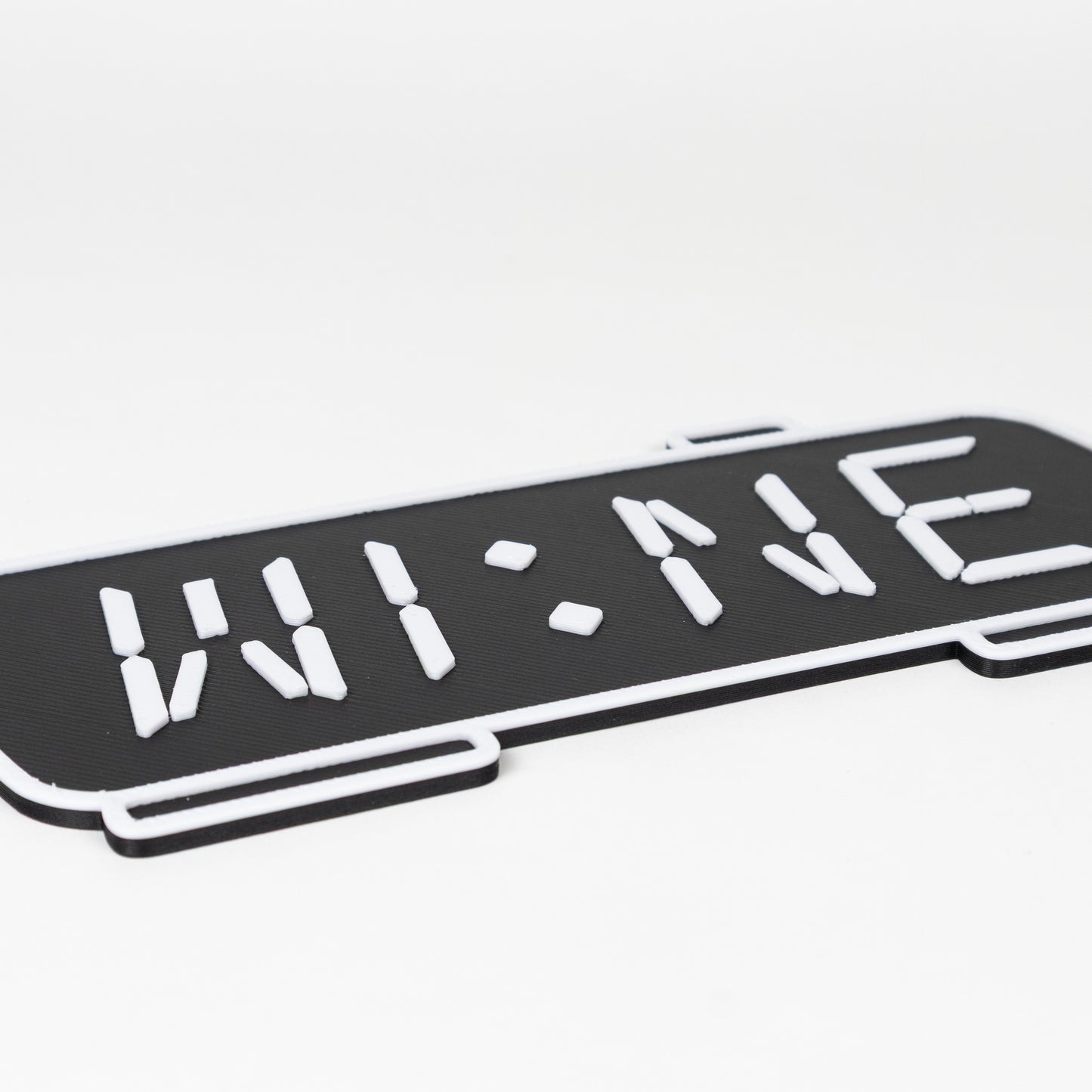 Close up of raised white text and outlines of a photo prop. Black and white sign of a digital clock displaying 'WINE'.