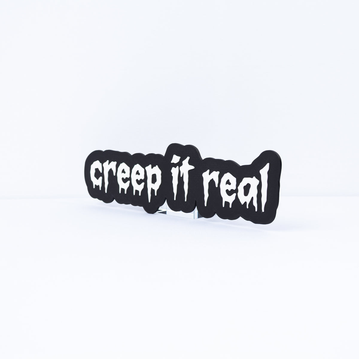 3D printed black sign with white stylized text that says, "creep it real". Shot on a white background at an angle.