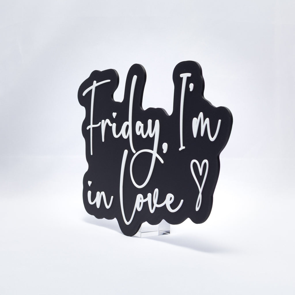 A 3D printed sign with white text on a black base that says, "Friday, I'm In Love" with a heart at the end. Shot at an angle on a white background.
