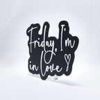 A 3D printed sign with white text on a black base that says, "Friday, I'm In Love" with a heart at the end. Shot at an angle on a white background.