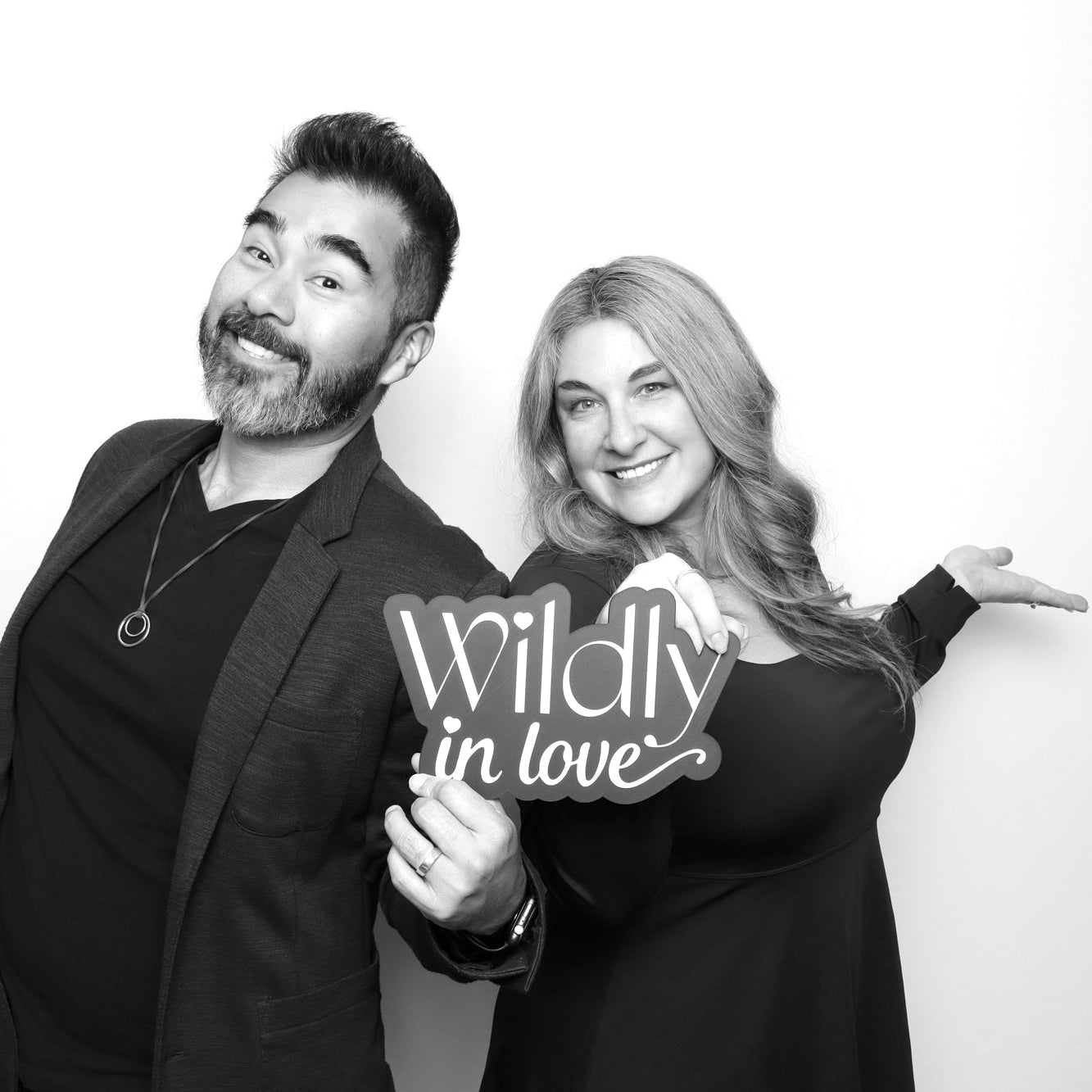 Two people posing with a 'Wildly in Love' sign in a black and white photo booth.
