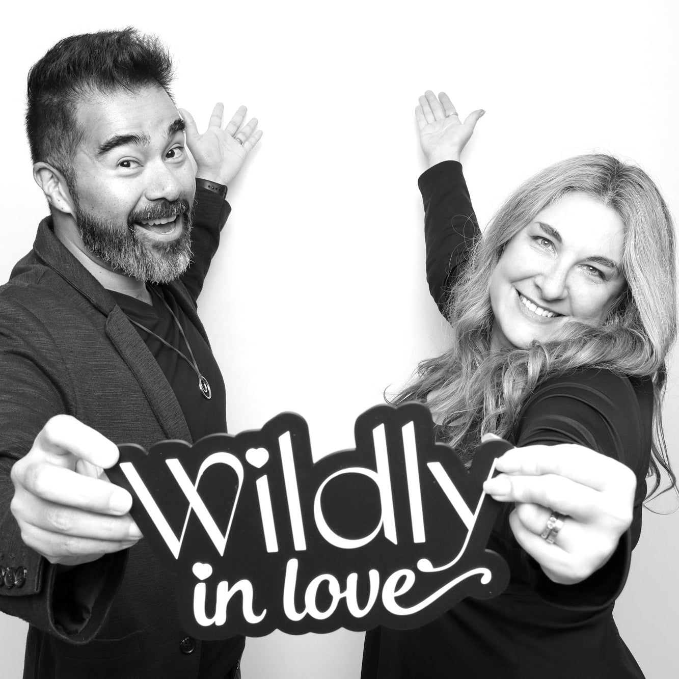 Black and white photo of a man and woman holding a 'Wildly in Love' sign in a photo booth.