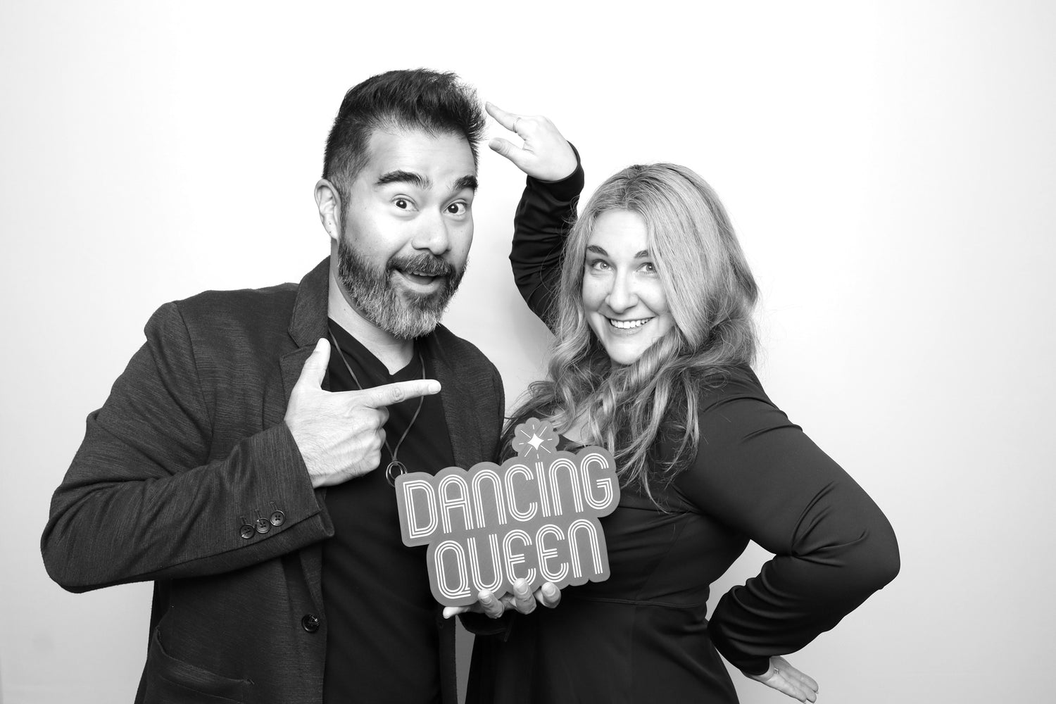 Two people posing with a 'Dancing Queen' sign in a black and white photo booth.