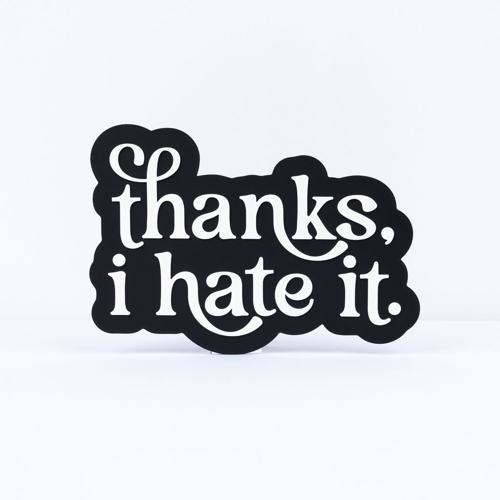 A black 3d printed sign with white text reading 'thanks, i hate it.' on a clean white background.