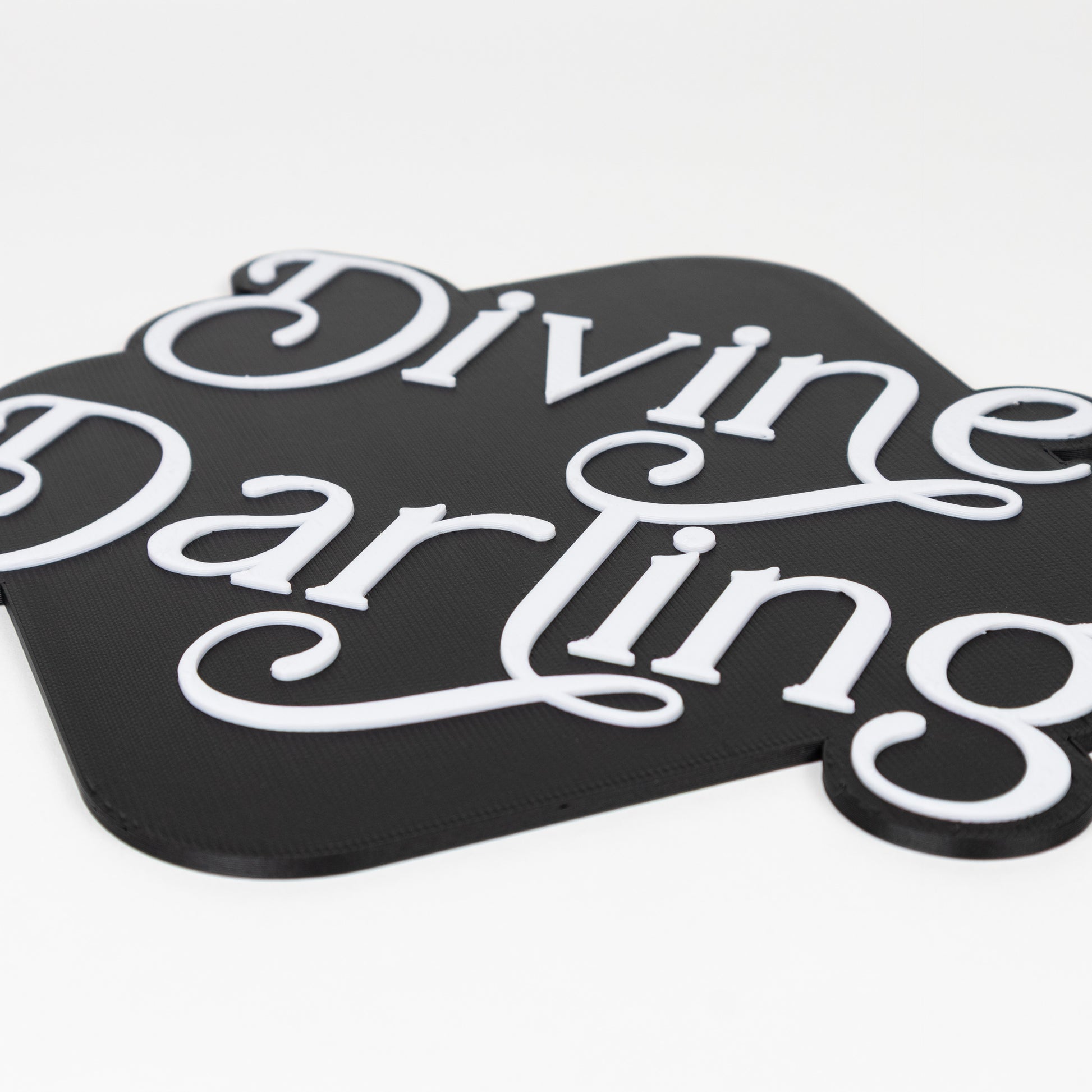 Black and white 'Divine Darling' photo booth prop sign on a white background. Close up shot of raised white lettering.
