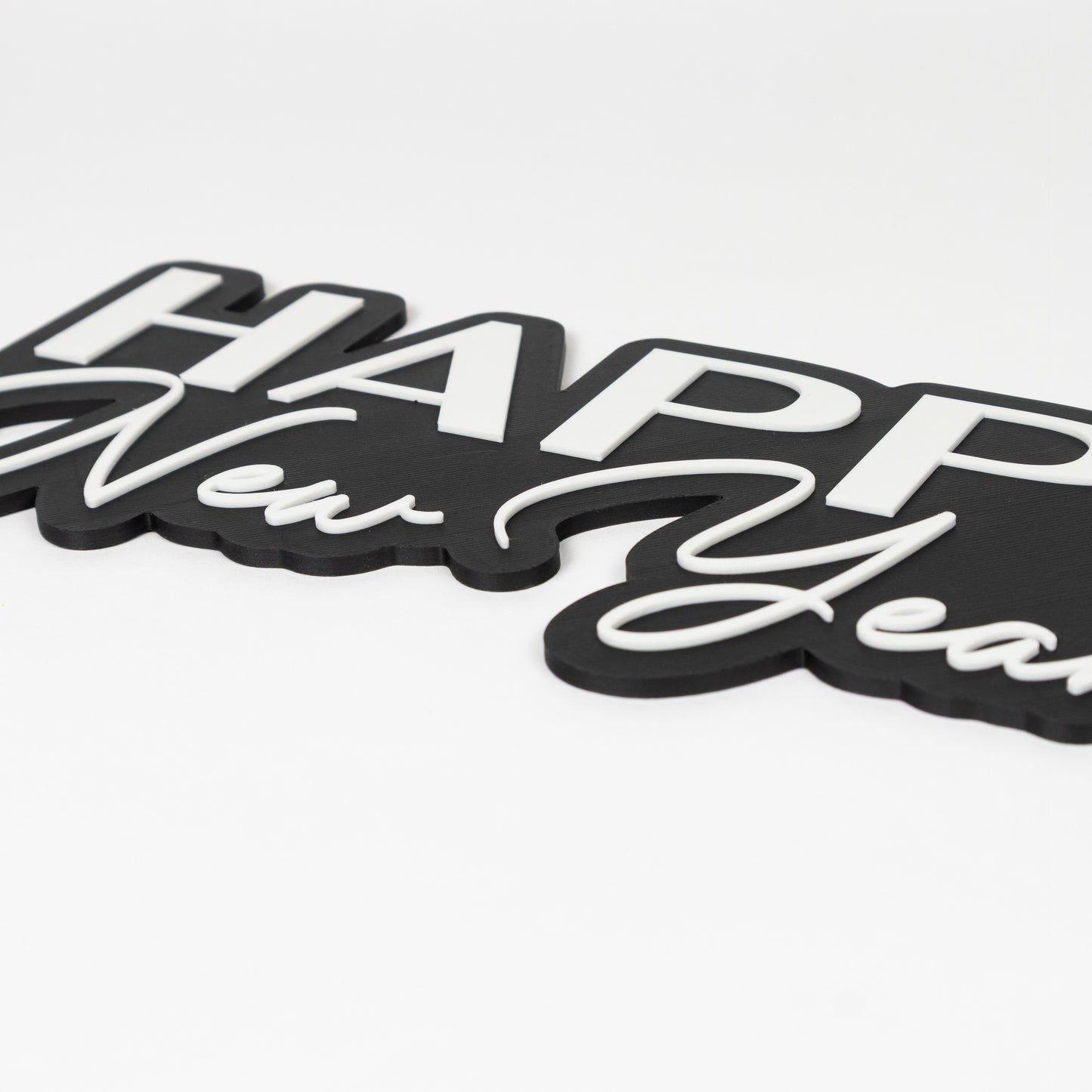 Close up shot of raised white text on a black base. Photo booth prop sign that reads "Happy New Year!"