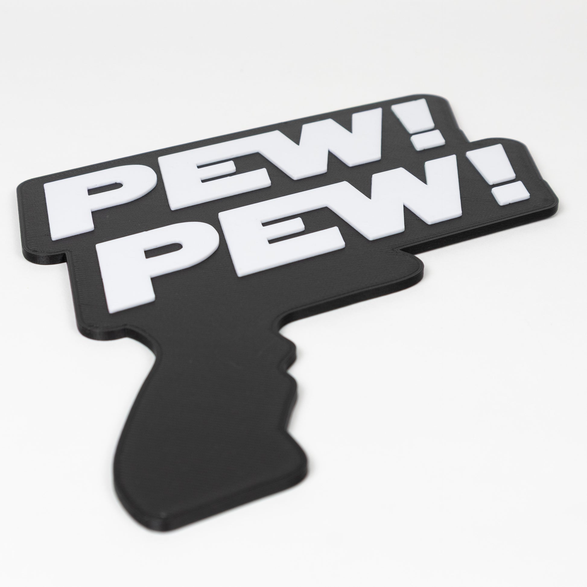 Close up of a black and white sign that says "Pew Pew!". Shows raised white text on a black base. Sign is in the shape of a Star Wars blaster. Photo booth prop.