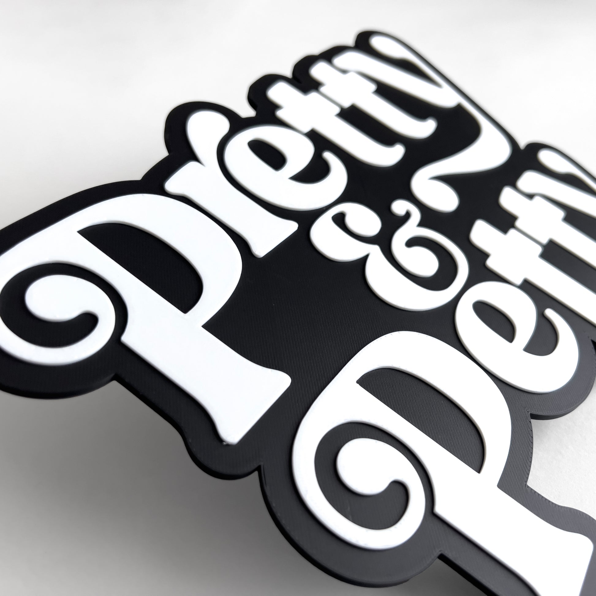 Close up of a black and white sign that says "Pretty and Petty". Shows raised white lettering.