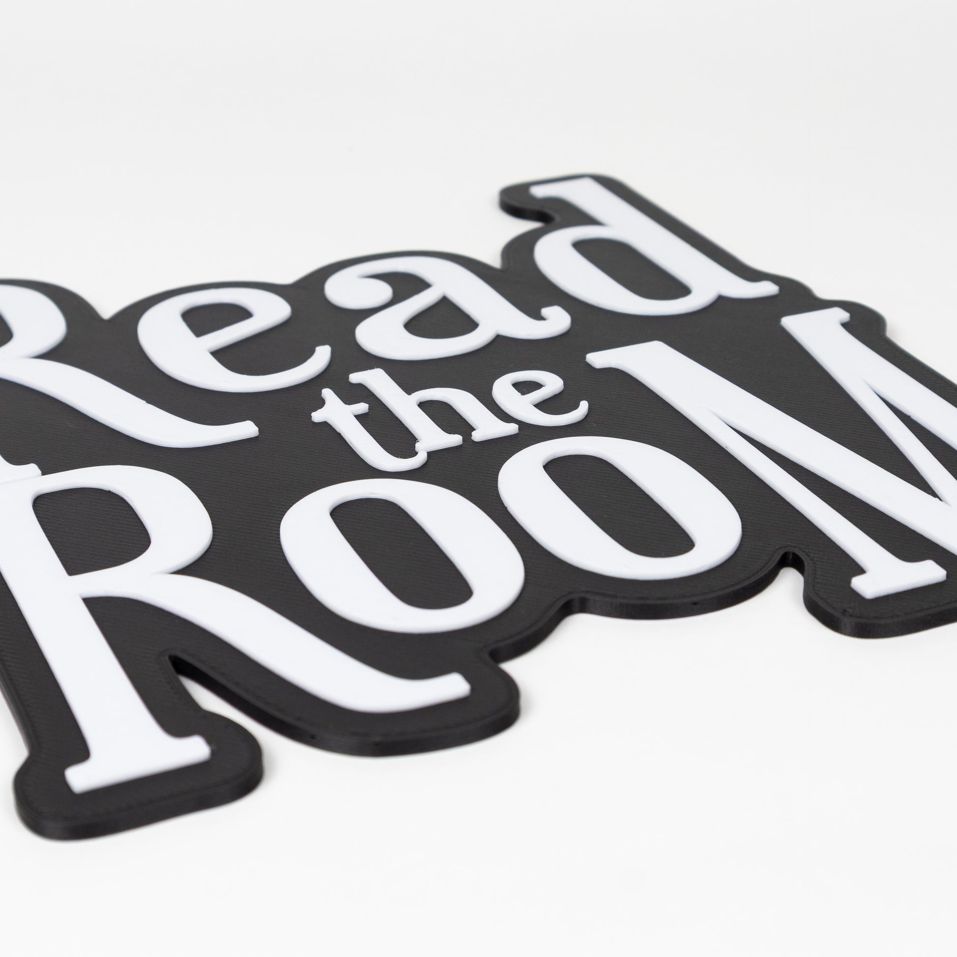 Close up of raised white text on a black base. Black and white "Read the Room" sign. Photo booth prop.
