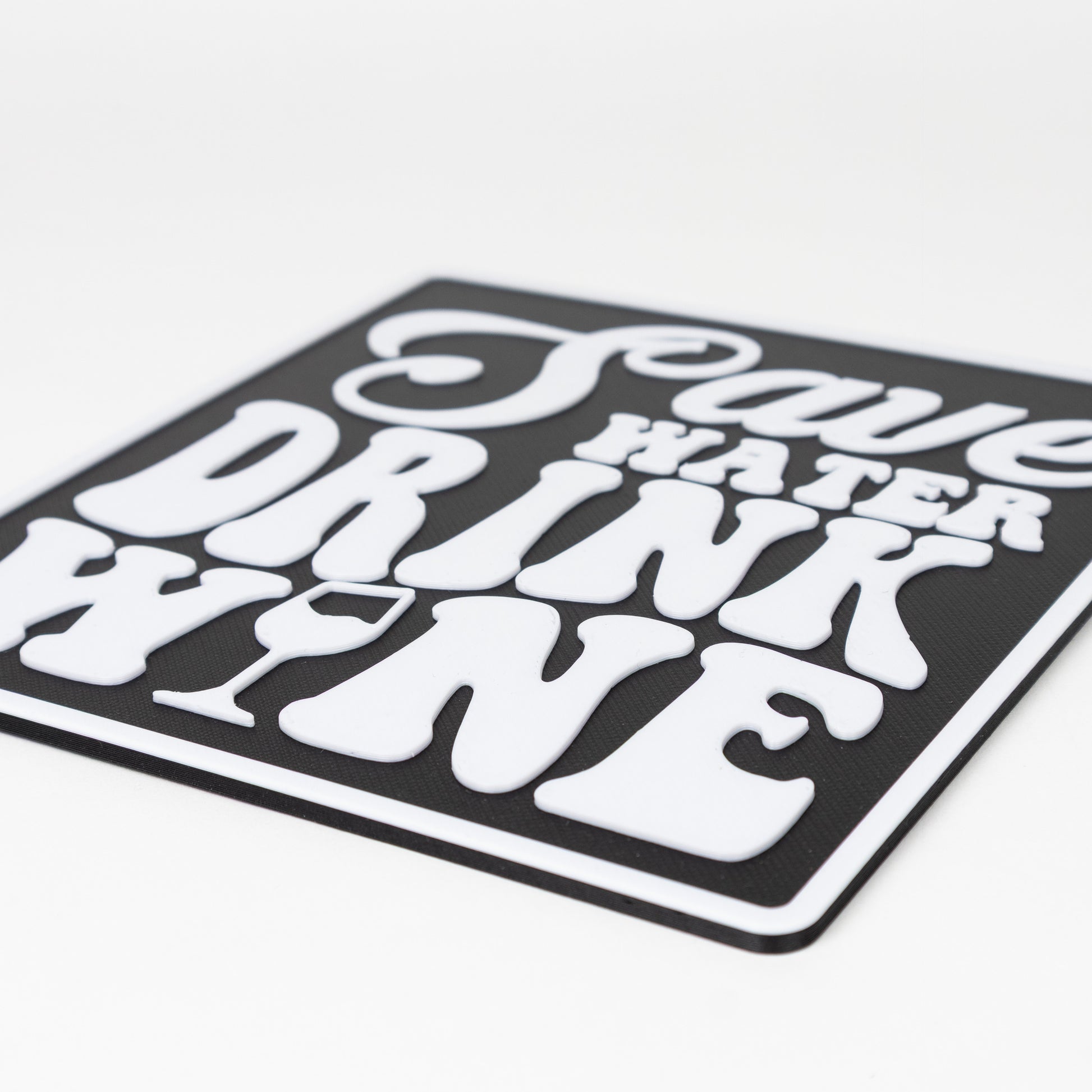 Close up of black and white sign that says, "Save Water, Drink Wine". Shows raised white text on a black silhouette base. Photo booth prop.