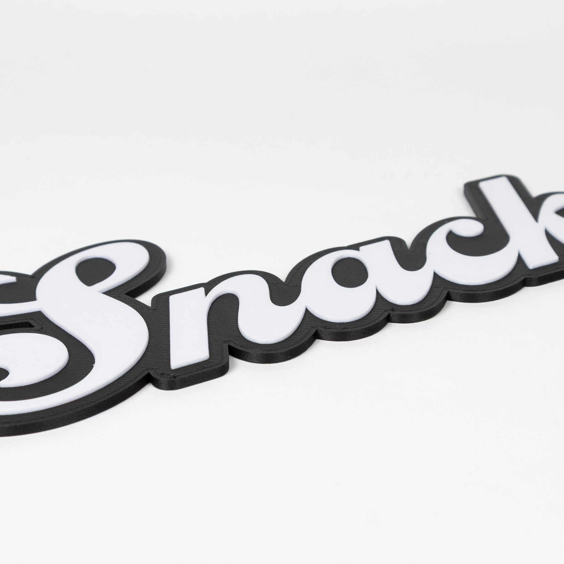 Close up of black and white flirty "Snack" sign. Shows raised white text on a black silhouette base. Photo booth prop.