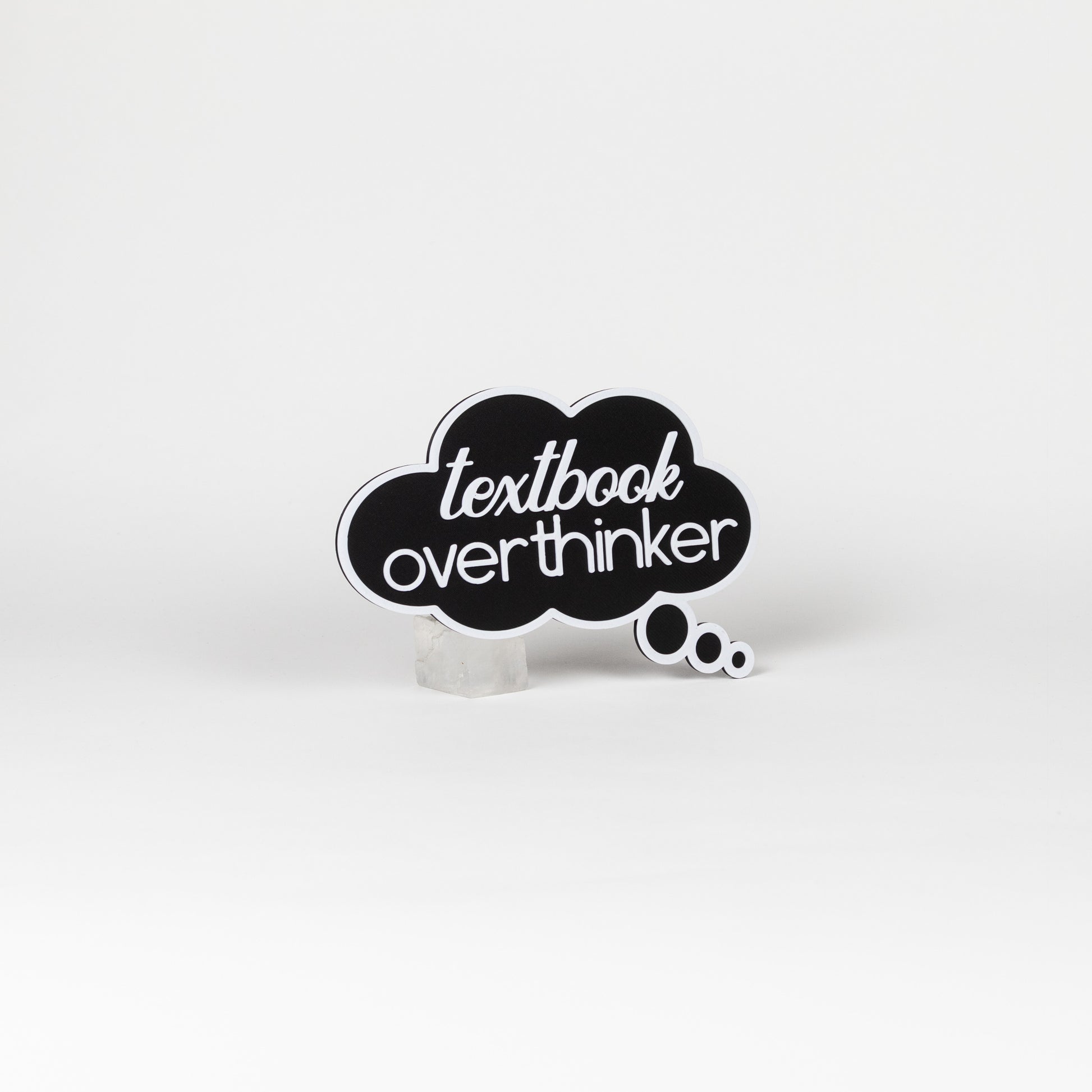 Black cloud-shaped sign with 'textbook overthinker' text in white. Photo booth prop shot on a white background.