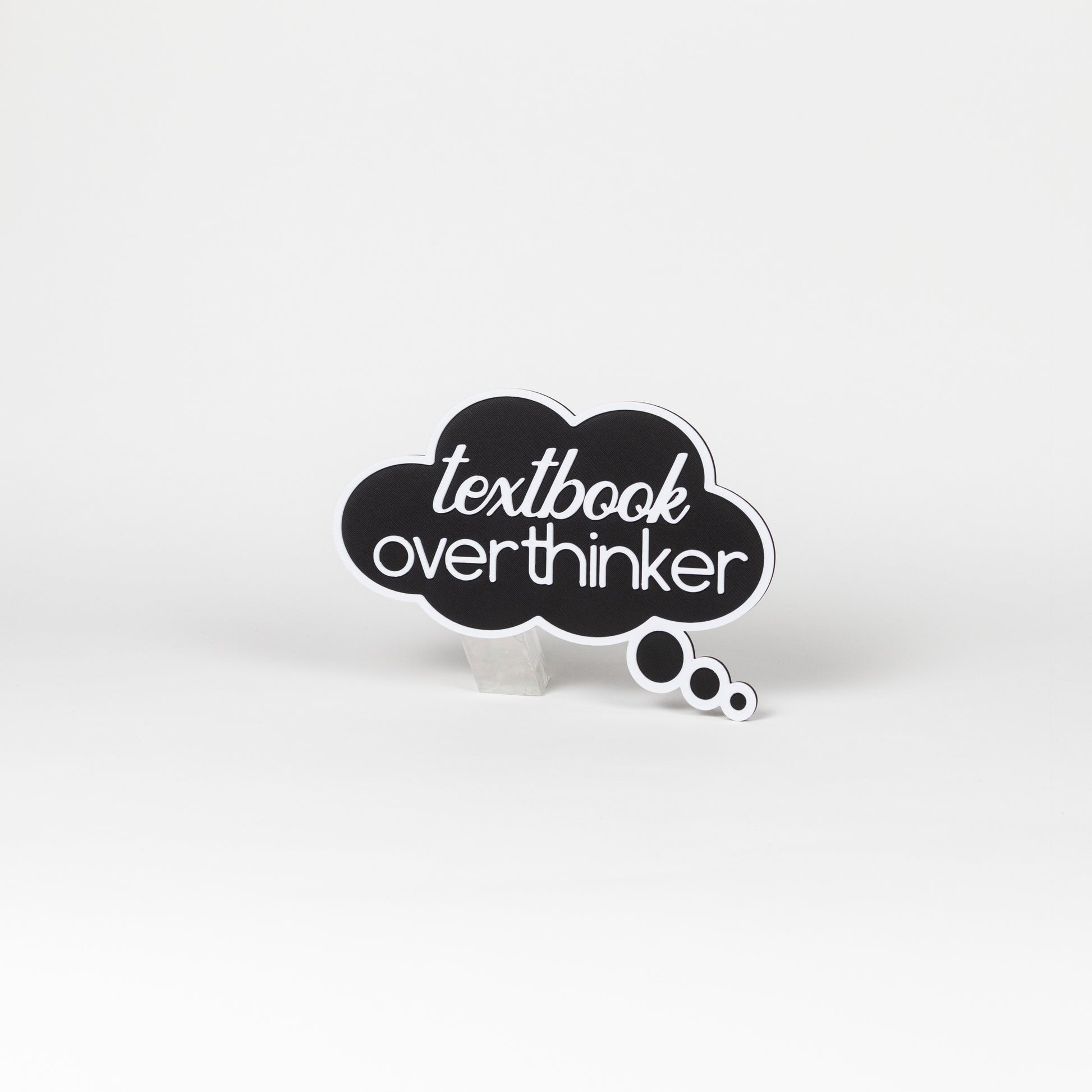 Black thought bubble sign with 'textbook overthinker' text in white. Photo booth prop shot on a white background.